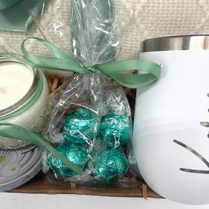 May include: A gift basket with a white mug, a candle, and a bag of green chocolate truffles tied with a green ribbon.