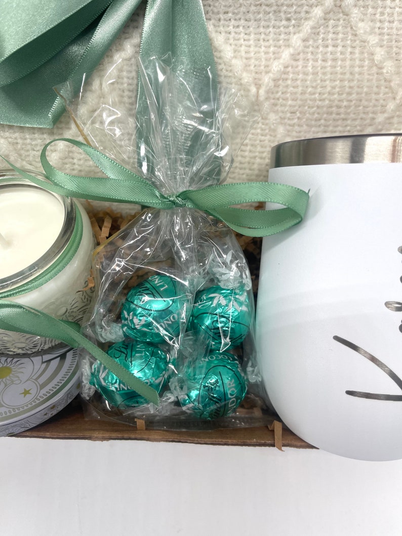May include: A gift basket with a white mug, a candle, and a bag of green chocolate truffles tied with a green ribbon.