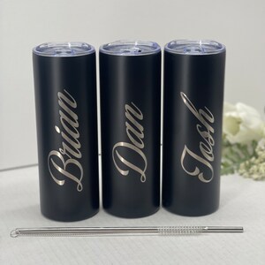 May include: Three black stainless steel tumblers with personalized names "Brian", "Dan", and "Josh" engraved in silver lettering. The tumblers are lined up in a row and come with a stainless steel straw.