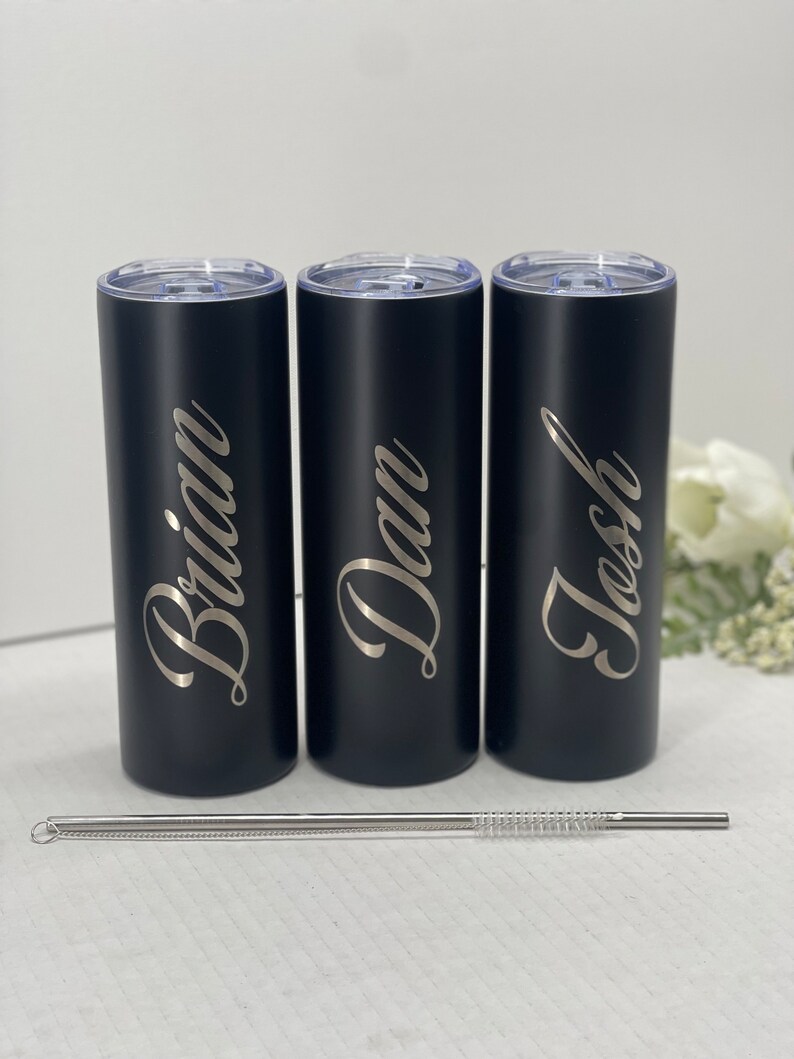 May include: Three black stainless steel tumblers with personalized names "Brian", "Dan", and "Josh" engraved in silver lettering. The tumblers are lined up in a row and come with a stainless steel straw.