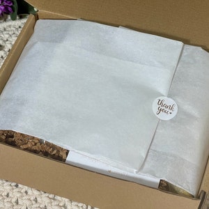 May include: A brown cardboard box with a white tissue paper liner and a round sticker that says "Thank you". The box is filled with brown packing peanuts.