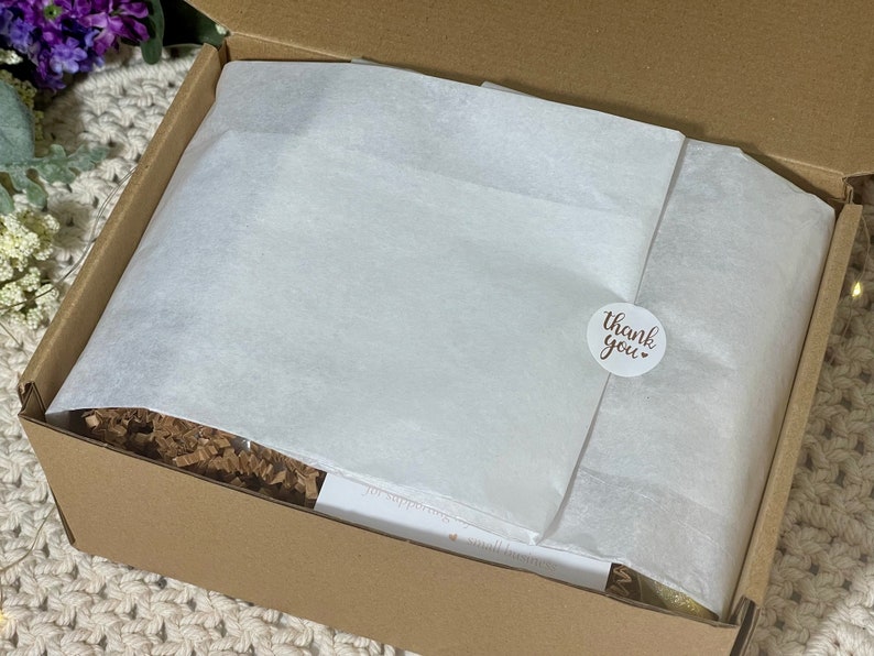 May include: A brown cardboard box with a white tissue paper liner and a round sticker that says "Thank you". The box is filled with brown packing peanuts.