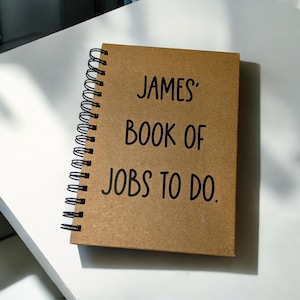 May include: A brown spiral bound notebook with the text "JAMES' BOOK OF JOBS TO DO." printed in black.