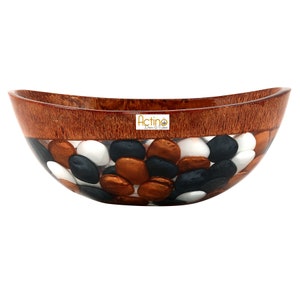 May include: An oval-shaped bowl made of wood and resin with a clear resin layer filled with black, white, and copper colored stones. The bowl has a brown wood rim and the text "Actino Decor & Shop" is visible on the bowl.
