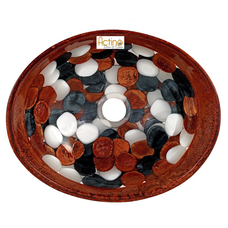 May include: Oval-shaped sink with a brown rim and a clear resin interior. The sink is decorated with white, black, and copper-colored pebbles.