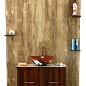 May include: A brown wooden bathroom vanity with a white countertop and a brown and white mosaic sink with a copper faucet. The vanity has two drawers with silver handles. There are shelves on the wall behind the vanity with various toiletries.