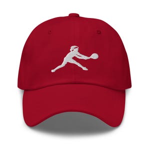 Può includere: Un cappello da baseball rosso con una silhouette ricamata bianca di una persona che gioca a tennis.