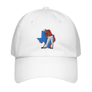 Op de afbeelding: Witte baseballpet met een geborduurd ontwerp van een golfer in een rood shirt en een witte broek die een golfclub zwaait voor een blauwe omtrek van de staat Texas.