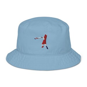 May include: A light blue bucket hat featuring an embroidered image of a person throwing a disc. The person is wearing a red shirt with a Union Jack design.
