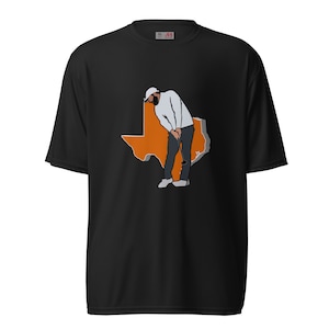 Puede incluir: Camiseta negra con un contorno naranja del estado de Texas. Un golfista de dibujos animados se representa dentro del contorno, vistiendo una camisa blanca, pantalones negros y una gorra blanca.