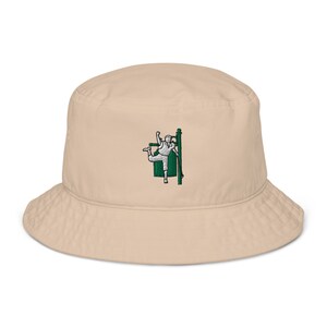 Op de afbeelding: Een beige bucket hat met een geborduurd beeld van een persoon in een groene outfit die een paal vasthoudt.