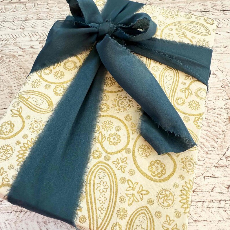 Gift wrapped in gold patterned paper with a blue ribbon on a textured surface