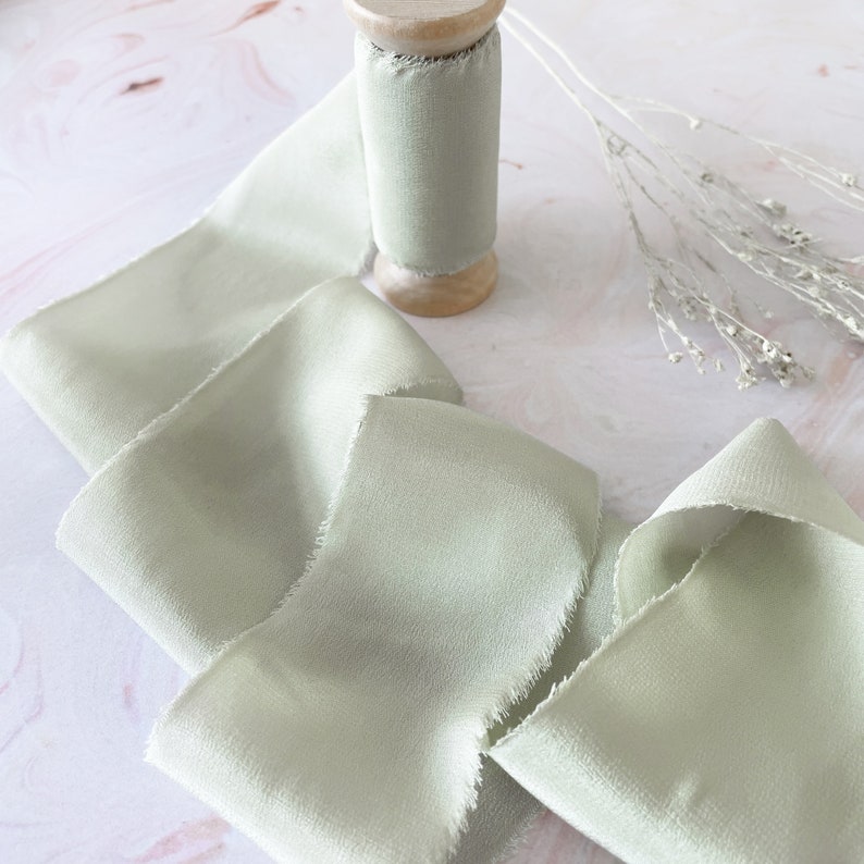 raw edge silk ribbon on dusky sage green.  Light green silk ribbon for wedding invitations and crafts.  Luxury ribbon on wooden spool