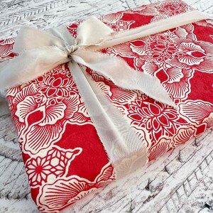 Red and white floral fabric with a beige ribbon on a textured surface