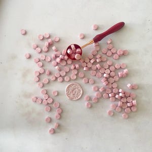 A collection of soft pink, pearlised sealing wax beads scattered on a surface with a red melting spoon above them.