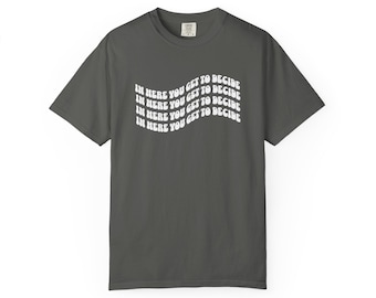 May include: Dark gray t-shirt with the text "IN HERE YOU GET TO DECIDE" in a wavy, white font. The shirt is a basic crew neck style, suitable for casual wear.