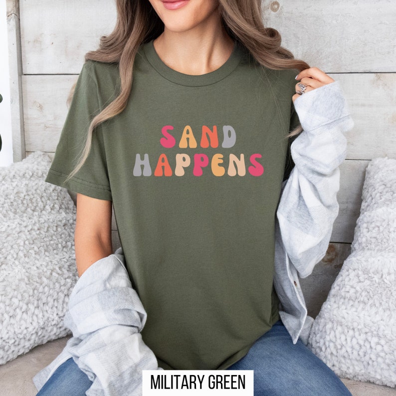 May include: A green t-shirt with the text "SAND HAPPENS" in colorful, retro-style lettering.