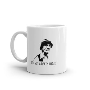May include: White ceramic mug with a black and white image of a man wearing a hat and the text "It's got a death curse!"