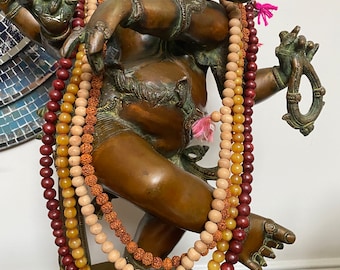 May include: A bronze statue of Ganesha, the Hindu god of wisdom and prosperity, adorned with three beaded necklaces in shades of red, brown, and yellow.