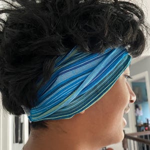 May include: A blue and white striped headband. The headband is made of a woven fabric and is wrapped around the head. The colors include shades of blue, green, and white. The headband is a hair accessory.