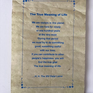 May include: A scroll with a blue border and text in blue that reads "The True Meaning of Life." The text continues with a quote about the meaning of life attributed to the Dalai Lama.