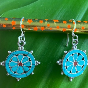 May include: A pair of silver earrings with turquoise and red flower designs. The earrings have a circular shape with a flower in the center and a silver hook.