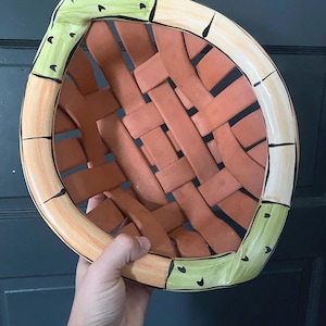 May include: A ceramic basket with a woven terracotta-colored body. The rim features alternating sections of light orange with black line accents and light green segments decorated with small black triangular markings along the outer edge.