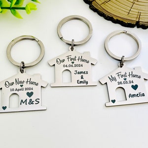 May include: Three silver house-shaped keychains with engraved text. The first keychain says "Our New Home" with the date "10 April 2024" and the initials "M&S". The second keychain says "Our First Home" with the date "04.04.2024" and the names "James & Emily". The third keychain says "My First Home" with the date "26.03.24" and the name "Amelia".
