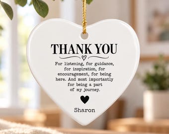 Puede incluir: Un adorno de cerámica blanco en forma de corazón que cuelga de un cordón dorado. El texto dice: THANK YOU. For listening, for guidance, for inspiration, for encouragement, for being here. And most importantly for being a part of my journey. Sharon.