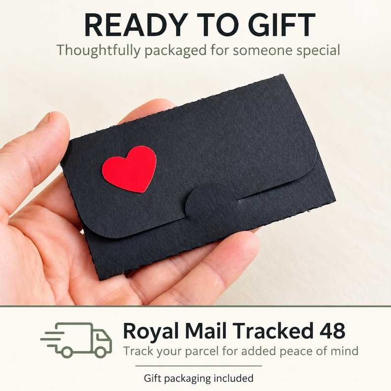 Puede incluir: Un sobre peque&ntilde;o y rectangular de papel negro con un coraz&oacute;n rojo recortado en la solapa frontal. El sobre tiene una superficie texturizada y un cierre de leng&uuml;eta redondeado. El texto READY TO GIFT y Royal Mail Tracked 48 es visible.