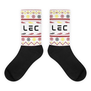 Könnte beinhalten: Ein Paar schwarze Socken mit einem weißen, roten und gelben Weihnachtsmuster. Das Muster enthält Schneeflocken, Rennwagen und das Wort "LEC".