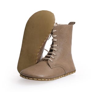 May include: Beige leather ankle boots with laces and a stitched seam around the sole.