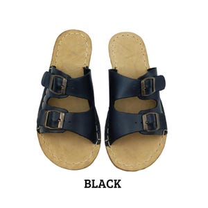 May include: A pair of black leather sandals with two adjustable buckle straps. The sandals have a light brown footbed and are labeled "BLACK" in bold, black text.