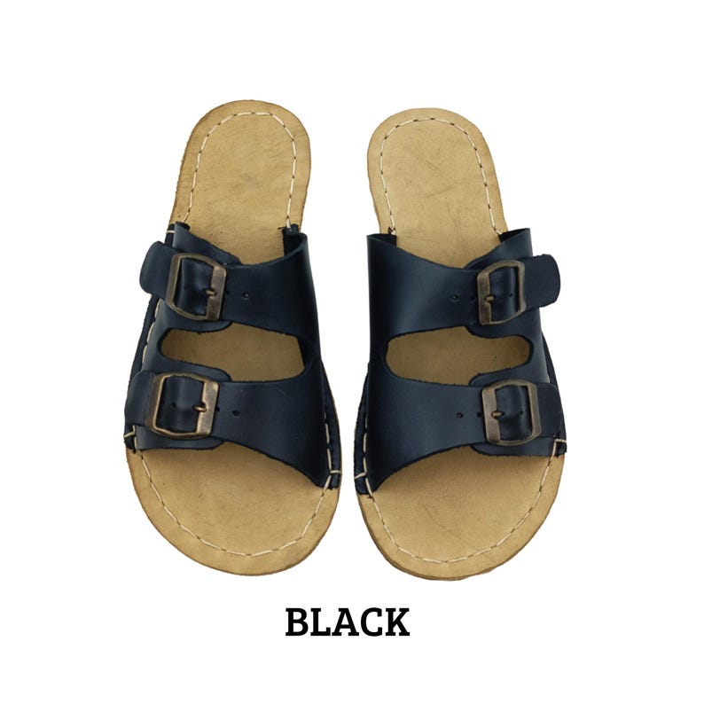 May include: A pair of black leather sandals with two adjustable buckle straps. The sandals have a light brown footbed and are labeled "BLACK" in bold, black text.