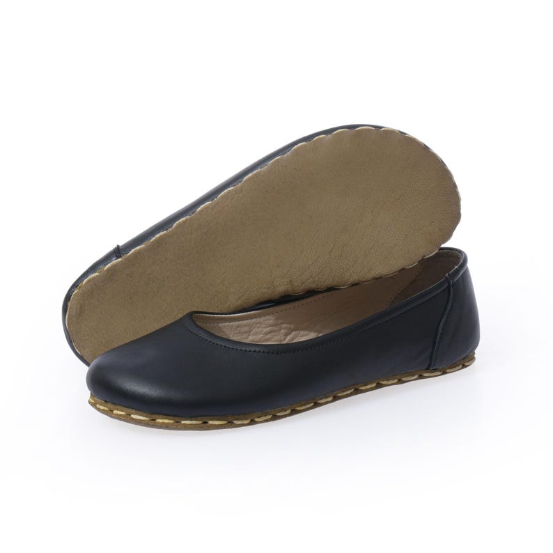 May include: A pair of black leather ballet flats with a brown stitched edge. The flats are shown with the insole facing up.