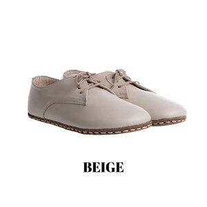 May include: A pair of beige lace-up shoes featuring a smooth finish, rounded toes, and visible stitching along the sole edge. The shoes have matching beige laces and a low-profile design. The word BEIGE is printed in black text below the shoes.