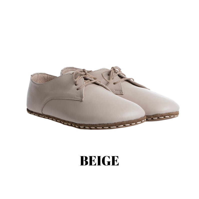 May include: A pair of beige lace-up shoes featuring a smooth finish, rounded toes, and visible stitching along the sole edge. The shoes have matching beige laces and a low-profile design. The word BEIGE is printed in black text below the shoes.