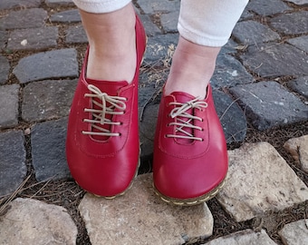 May include: A pair of red leather lace-up shoes with beige laces. The shoes are on a stone path.