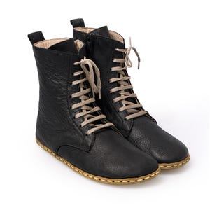 May include: Black leather lace-up ankle boots with a beige lace and a stitched sole.