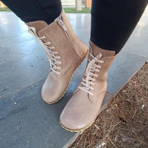 May include: Beige leather lace-up boots with a zip on the side. The boots have a flat sole and a slightly pointed toe.