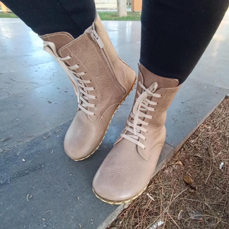 May include: Beige leather lace-up boots with a zip on the side. The boots have a flat sole and a slightly pointed toe.