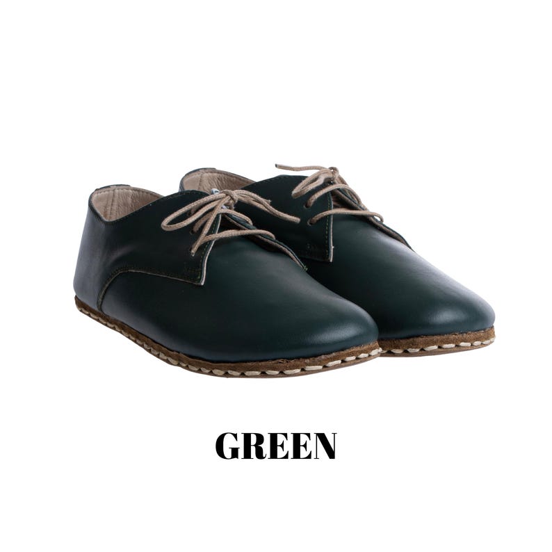 May include: A pair of dark green low-top shoes with beige laces and visible light-coloured stitching along the sole. The shoes feature a smooth finish and a rounded toe design. The word GREEN is printed in bold black capital letters below the shoes.