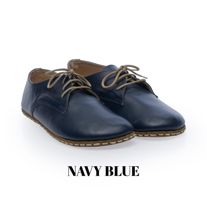 May include: A pair of navy blue leather shoes with a smooth finish, featuring beige laces and visible light-coloured stitching along the sole edge. The shoes have a rounded toe and a low-profile design. The text NAVY BLUE is printed below.