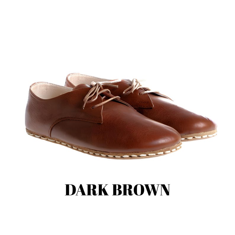 May include: A pair of dark brown leather shoes with a low-cut profile, rounded toes, and thin beige laces. The shoes feature visible light-coloured stitching along the sole edge and a smooth finish. The text DARK BROWN is printed below the shoes.