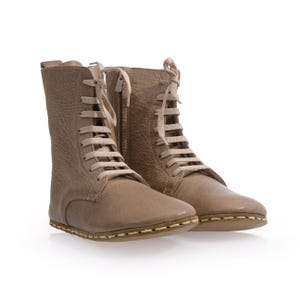 May include: A pair of beige leather ankle boots with lace-up fastenings and a stitched seam around the sole.