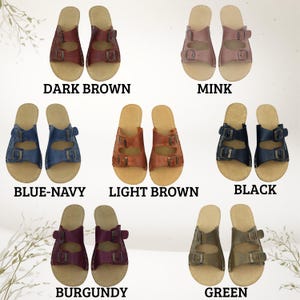 May include: Pairs of leather sandals in various colors, including dark brown, mink, blue-navy, light brown, black, burgundy, and green. Each sandal features a double-strap design with buckle closures and a light-colored footbed. The color names are displayed below each pair.