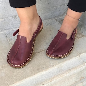 May include: Burgundy leather slip-on sandals with a stitched trim and a back strap.