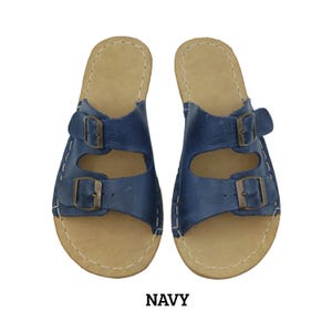 May include: Navy blue leather sandals with two adjustable buckles. The sandals have a light brown footbed and white stitching around the edges. The word "NAVY" is printed in a dark brown font at the bottom of the image.