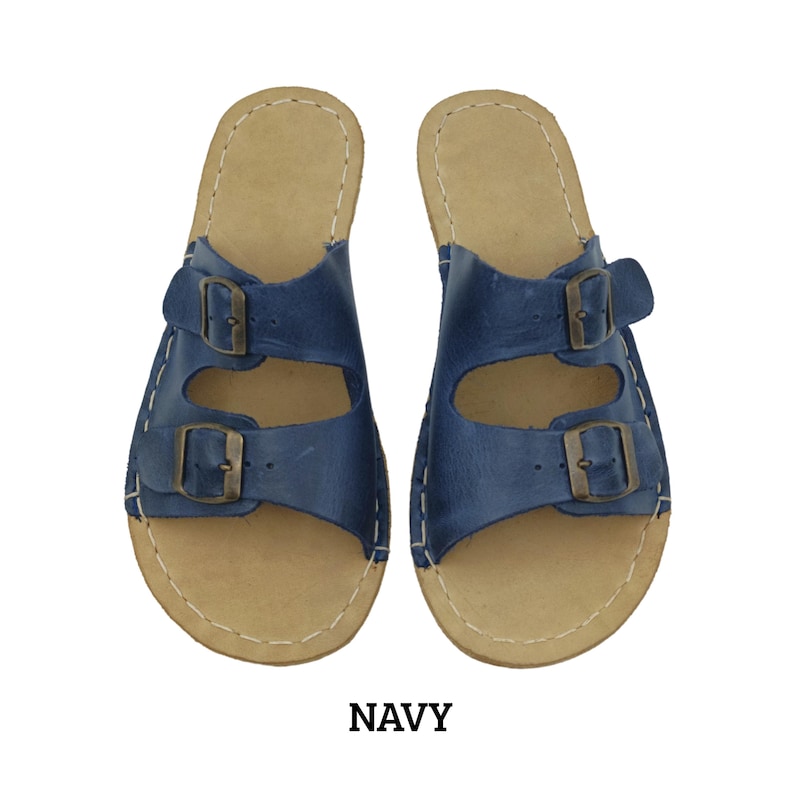 May include: Navy blue leather sandals with two adjustable buckles. The sandals have a light brown footbed and white stitching around the edges. The word "NAVY" is printed in a dark brown font at the bottom of the image.
