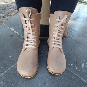 May include: A pair of light brown leather boots with white laces. The boots have a rounded toe and a low heel.